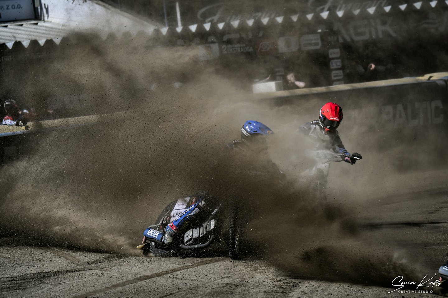 Two motorcycle racers speed through a cloud of dirt track dust.